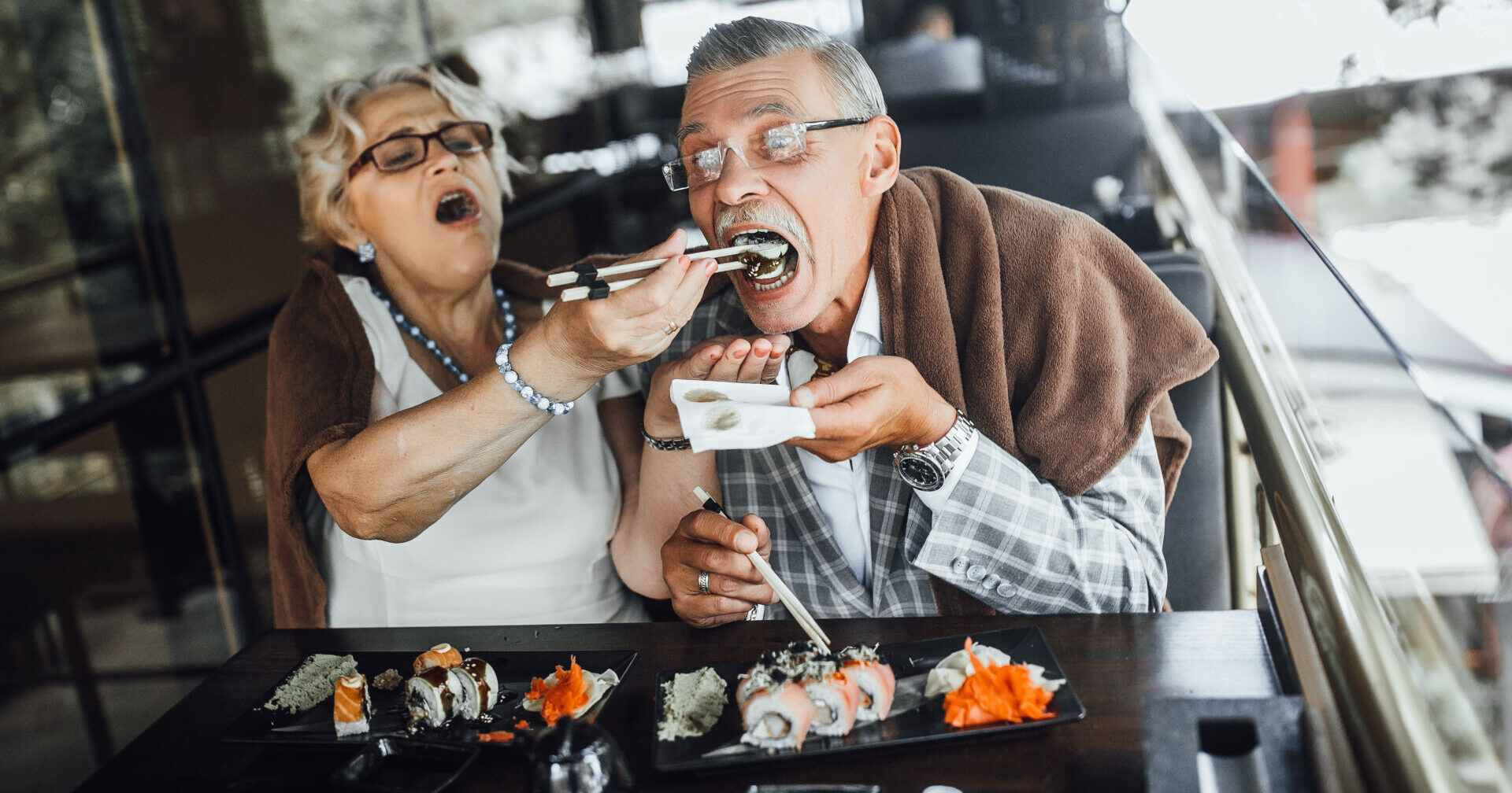 Lovely seniors couple eating sushi with red fish and sitting at summer terrace Lovely seniors couple eating sushi with red fish and sitting at summer terrace